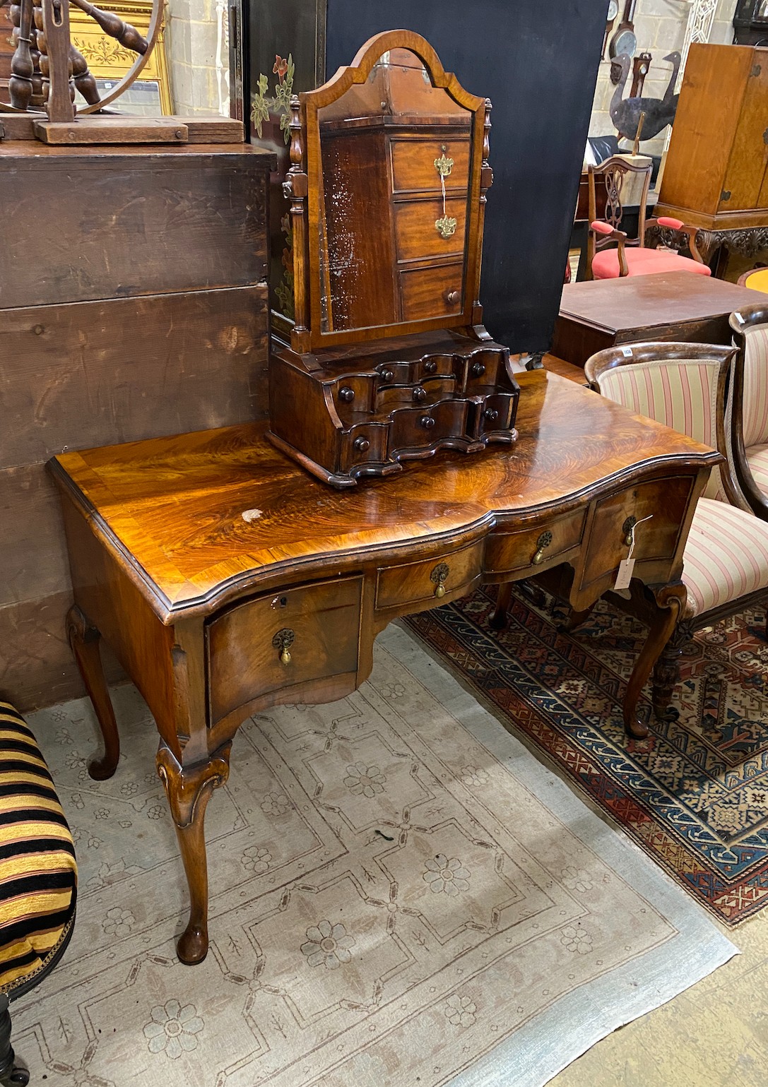 A Queen Anne Revival serpentine walnut kneehole dressing table, width 121cm, depth 54cm, height 76cm and a similar walnut toilet mirror